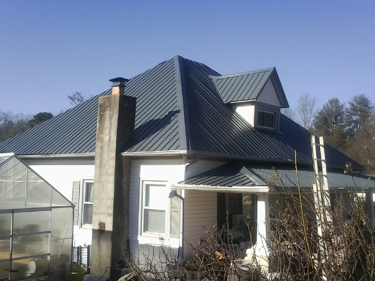 Dark blue standing seam metal roof on a white farmhouse with dormer — Slate & Tile Roof Repair by Roofing Brothers in Cove