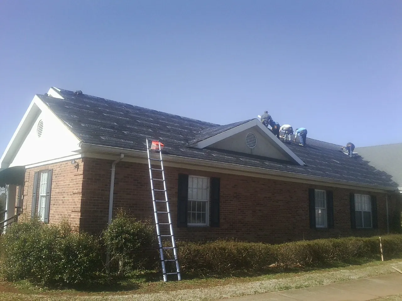 Crew tearing shingles off a brick ranch roof with a ladder set — Metal Roof Repair work by our crew in Cove