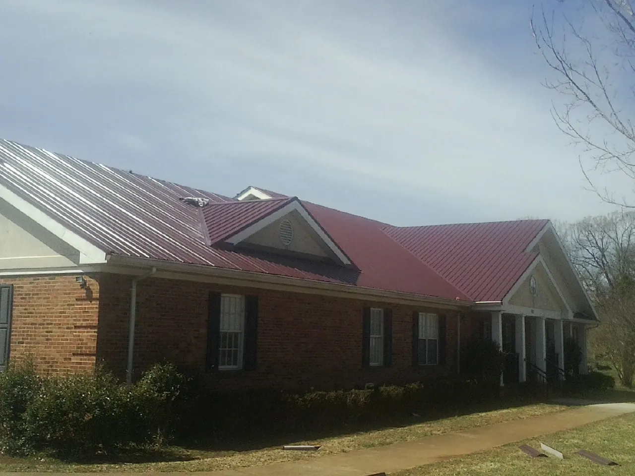 Red metal roof with gabled entries on a long brick building, from a Hail Damage Roof Repair job in Cove