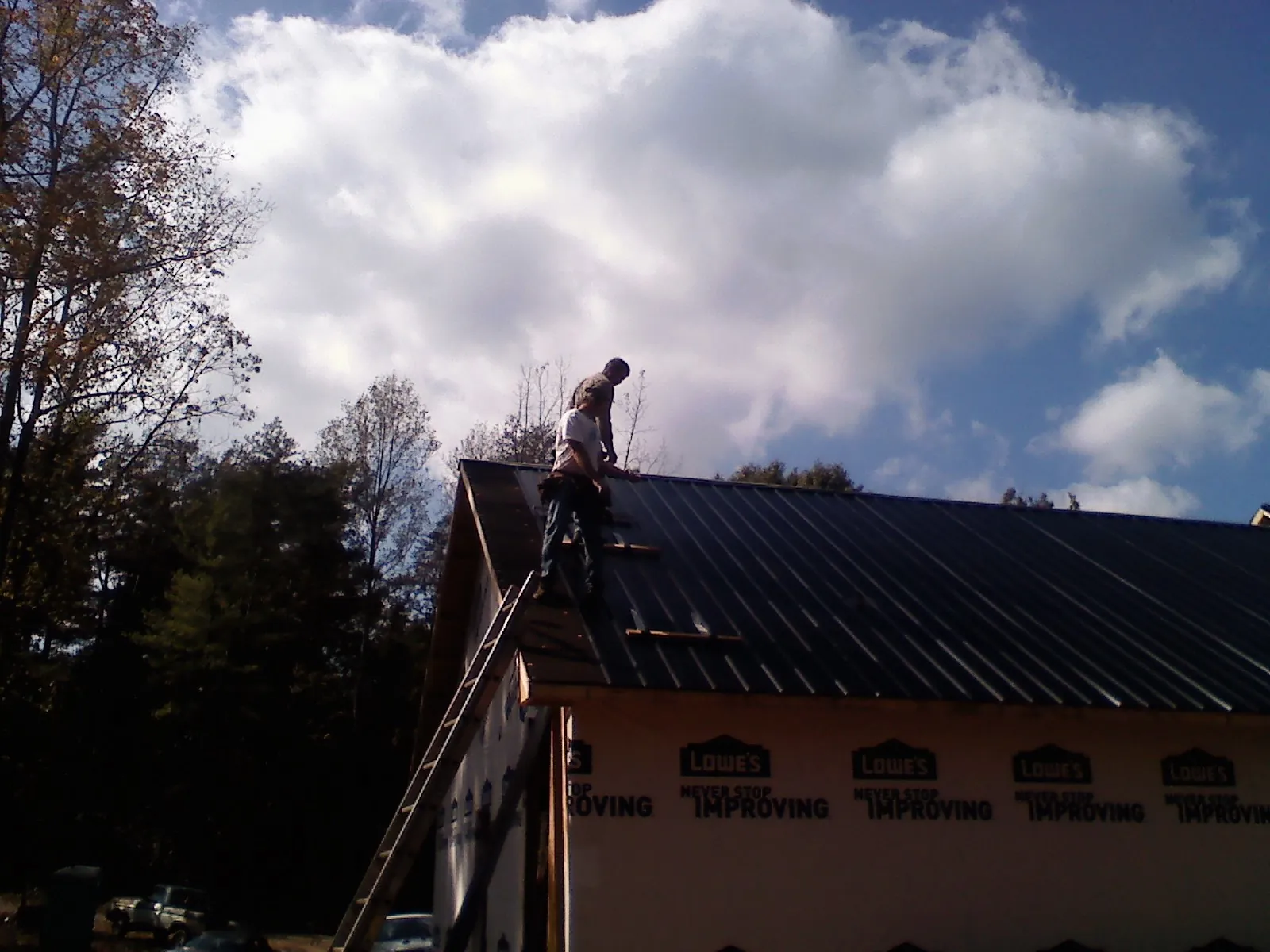 Roofer fastening dark metal panels high against a cloudy sky, from a Roof Inspection job in Cove