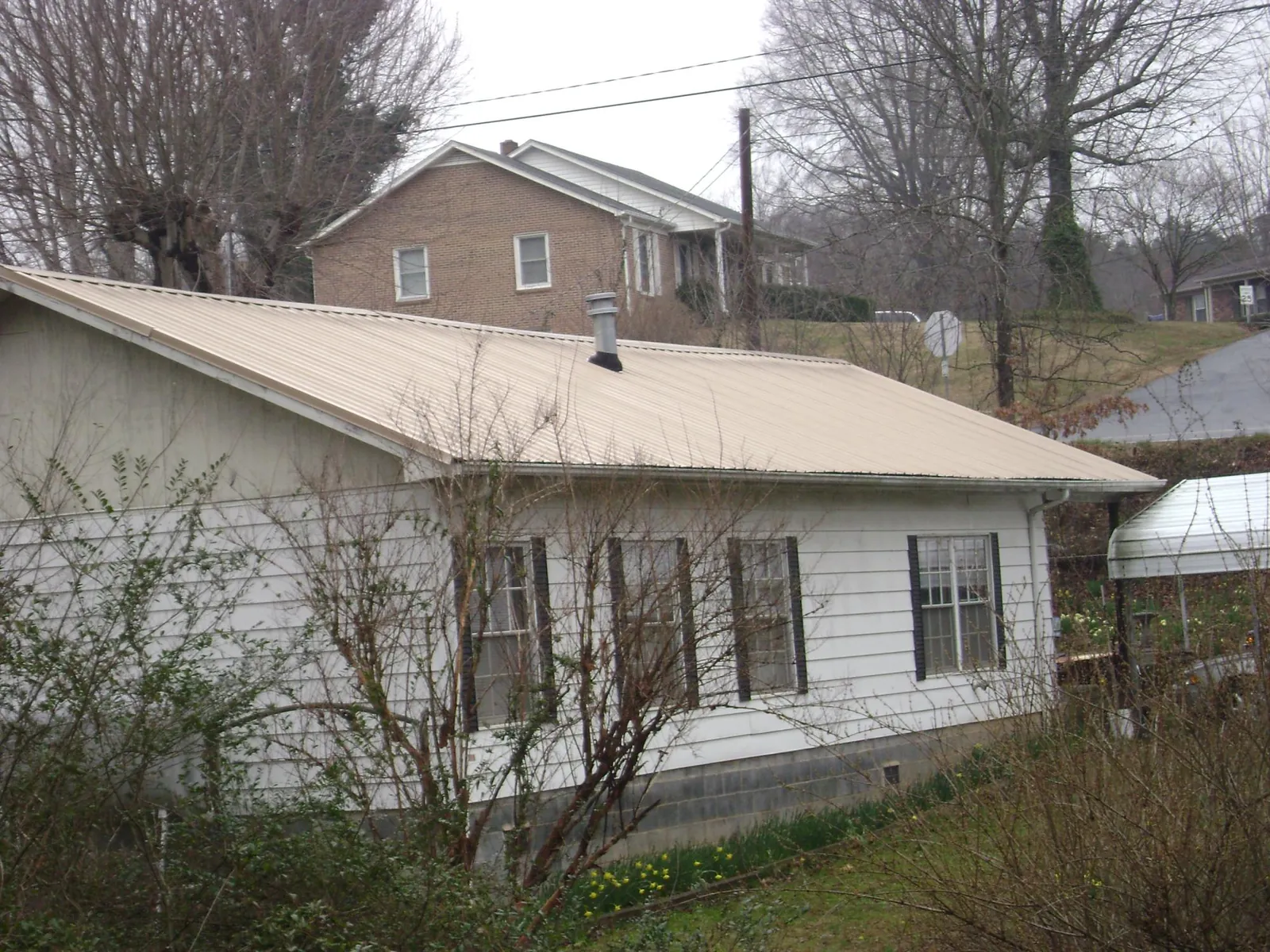 Tan metal roof on a white sided house set into a hillside — Commercial Roofing by Roofing Brothers in Cove
