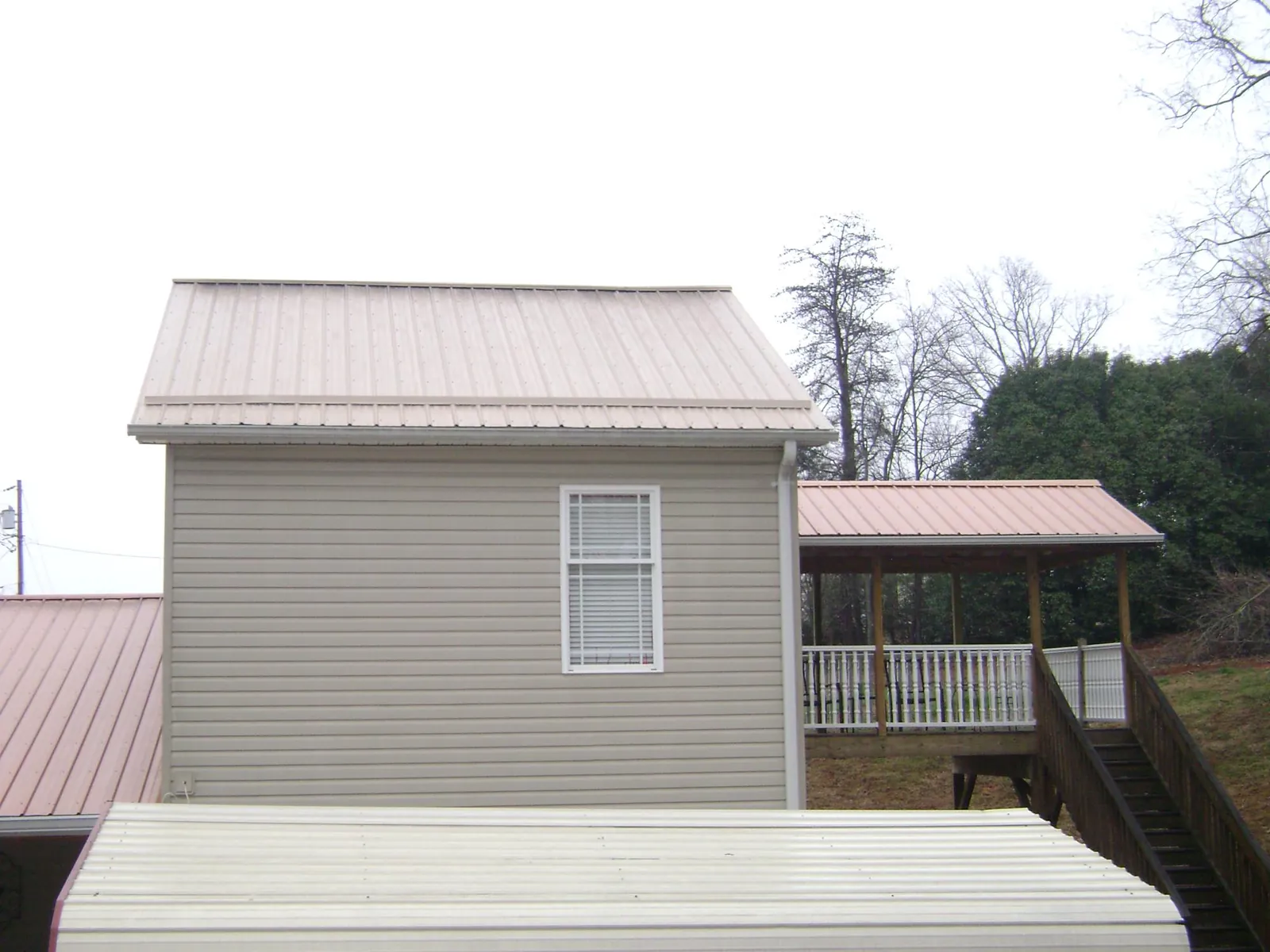 Tan metal roofs on a two story addition and attached porch, from a Roof Replacement job in Cove
